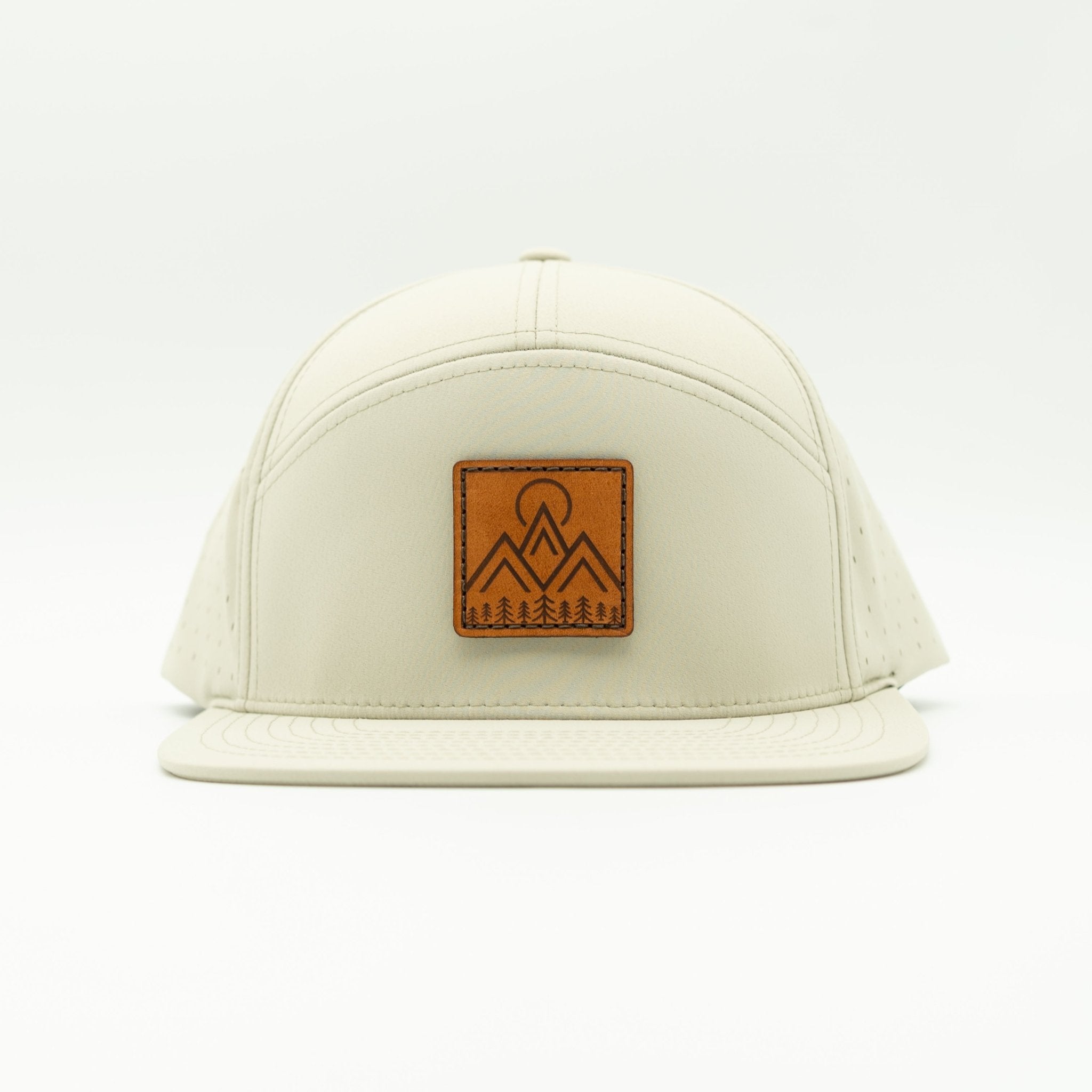 An off-white structured baseball cap with a brown leather patch on the front featuring a mountain and tree logo, set against a plain white background.

Color: Ivory