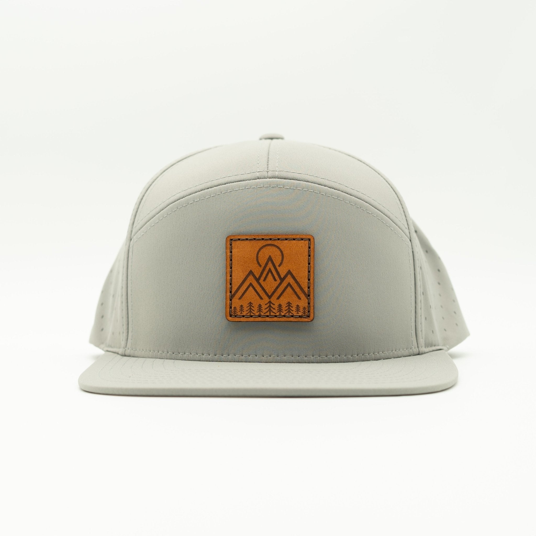 A light gray flat-brim cap with a brown leather patch on the front featuring a mountain and tree logo, photographed against a clean white background.

Color: Silver