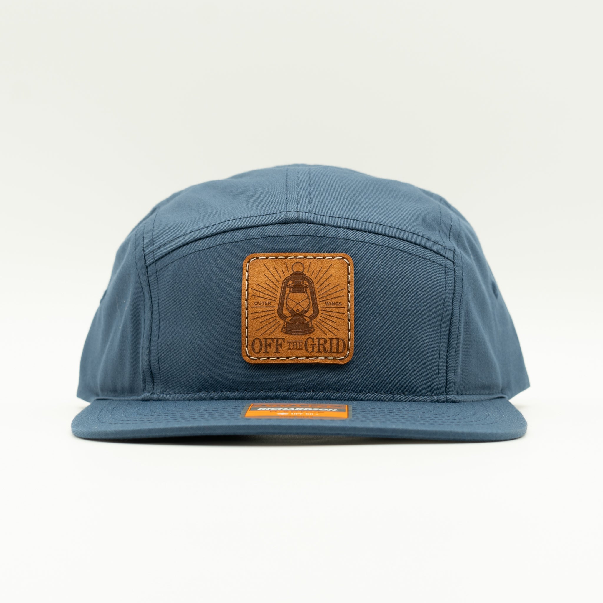 Light navy Off The Grid leather patch camper hat front view, Richardson 217 five panel with sewn veg tan patch and flat bill.