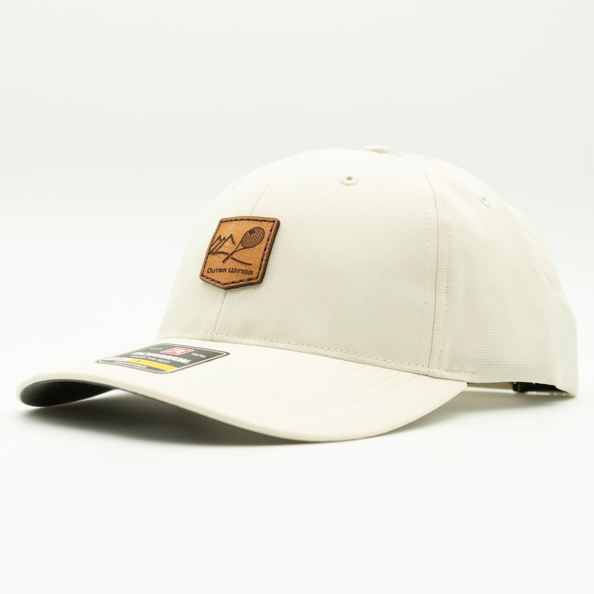 An off-white baseball cap with a brown rectangular patch on the front featuring a mountain and paddle graphic, with a small sticker on the brim, set against a plain white background.

Color: Stone