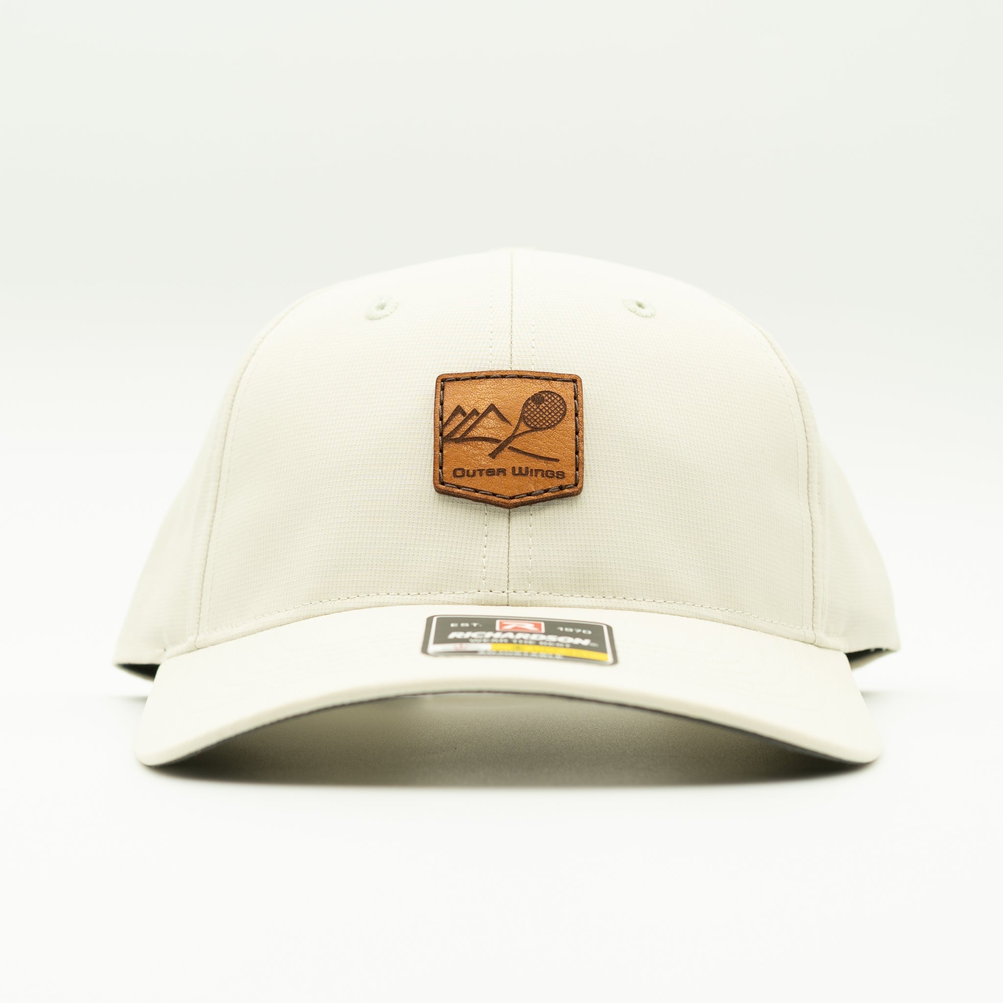 An off-white baseball cap with a brown leather patch on the front featuring a mountain and paddle graphic, with a brand label on the brim, set against a plain white background.

Color: Stone