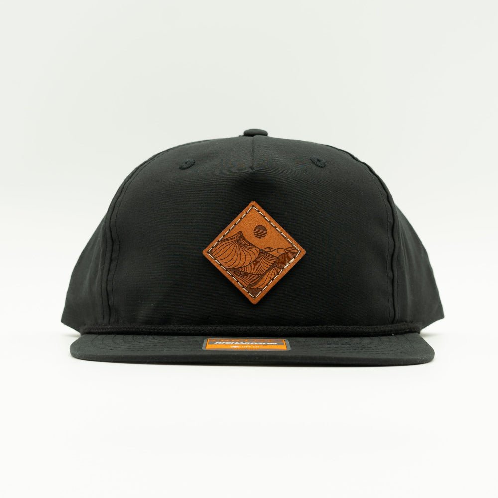 Front of black Richardson 256 Desert Mountain rope hat showing square veg-tan leather mountain patch, rope accent, and flat bill.

Color: Black
