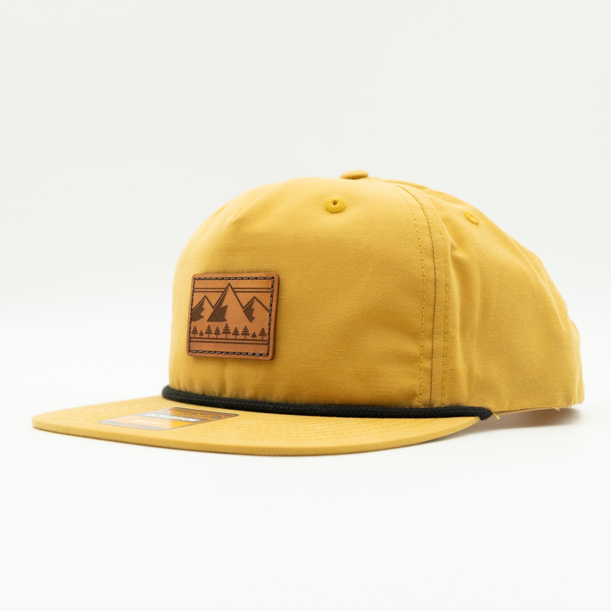 Side view of biscuit Richardson 256 Ridgeline mountain rope hat, showing tan fabric, leather mountain patch, flat rope bill, and low profile 5-panel shape.