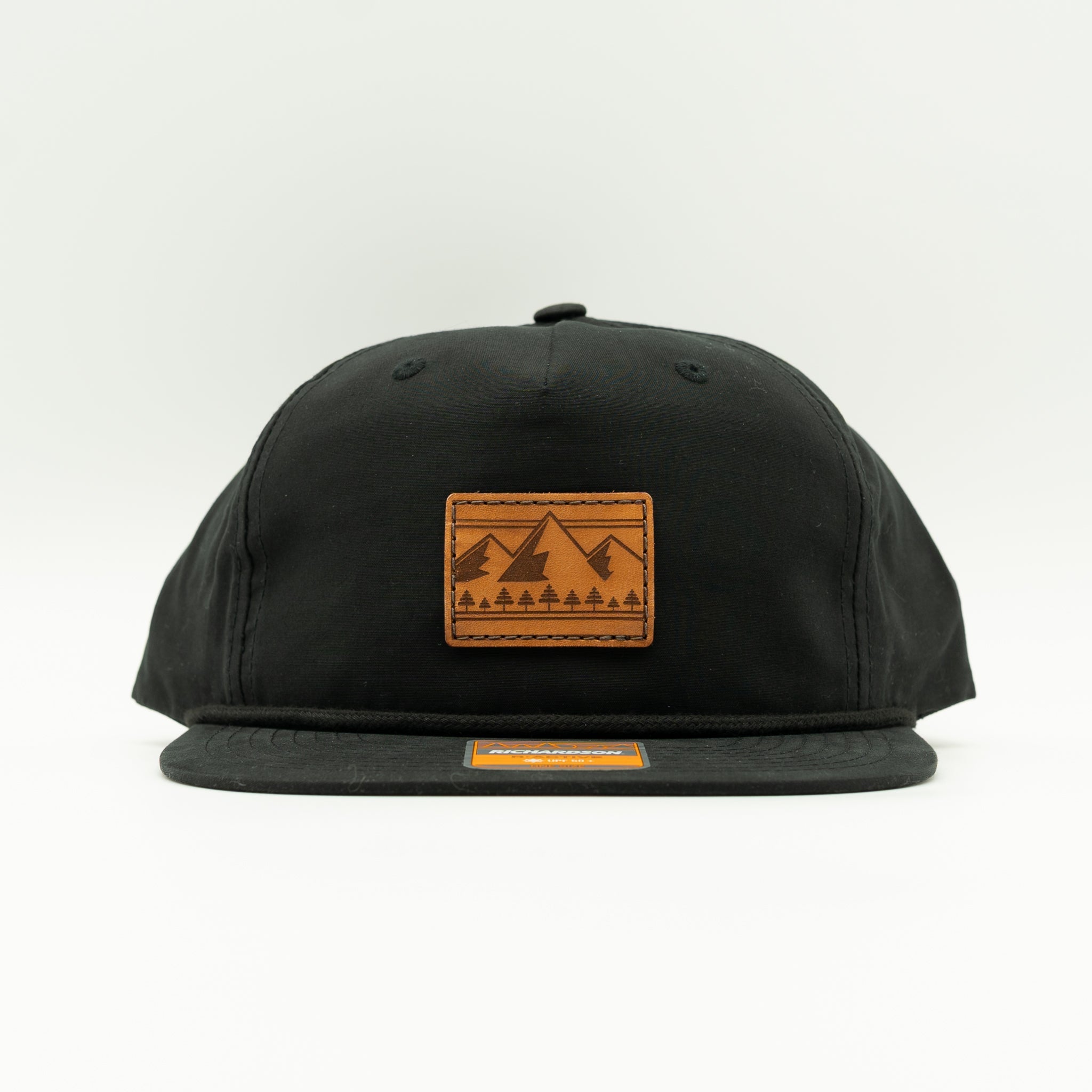 Front view of black Richardson 256 Ridgeline rope hat with square leather mountain and pine patch, flat bill with rope, lightweight cotton-nylon mountain hat.