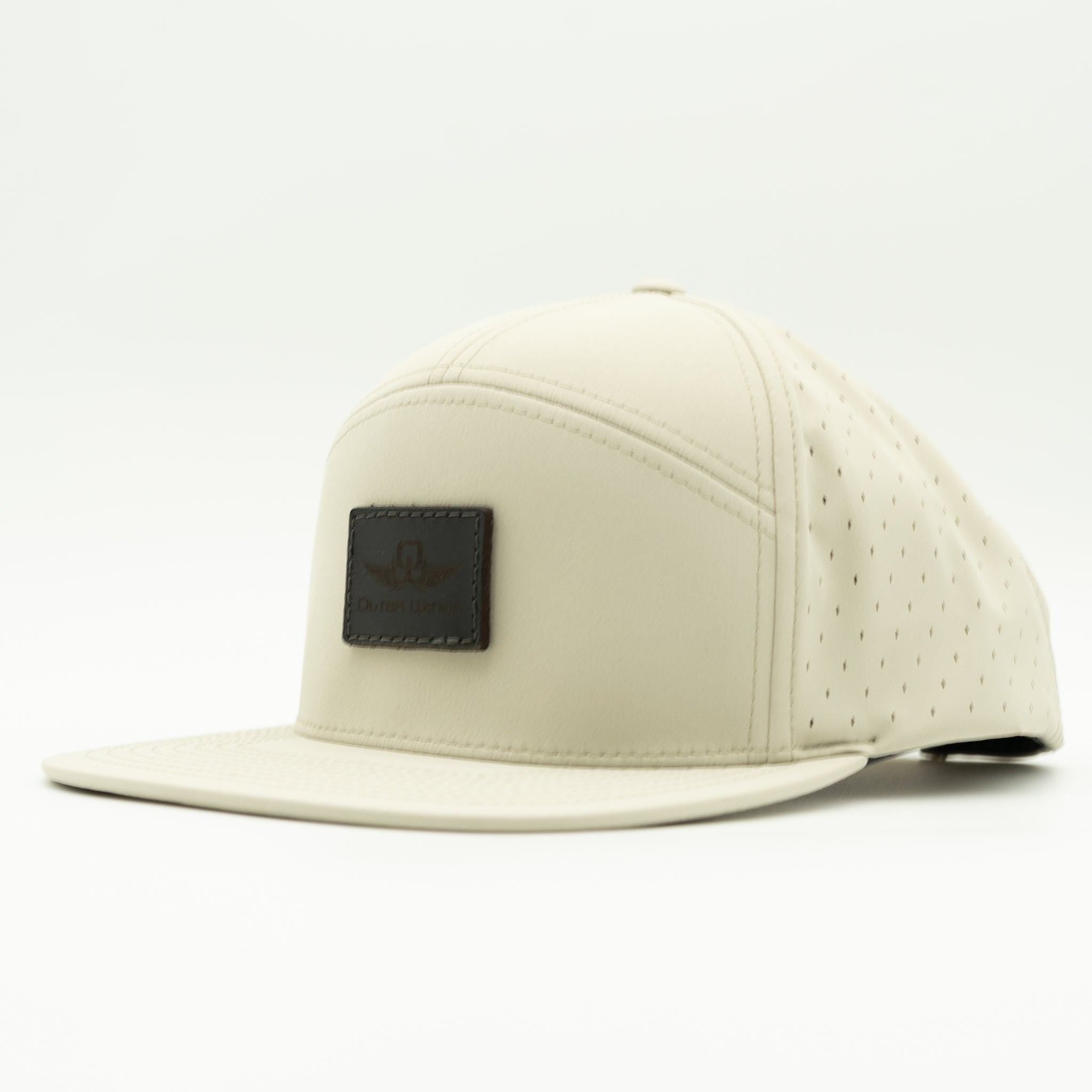 A light beige flat-brim cap with perforated side panels and a dark brown rectangular logo patch on the front, shown against a plain white background.

Color: Ivory