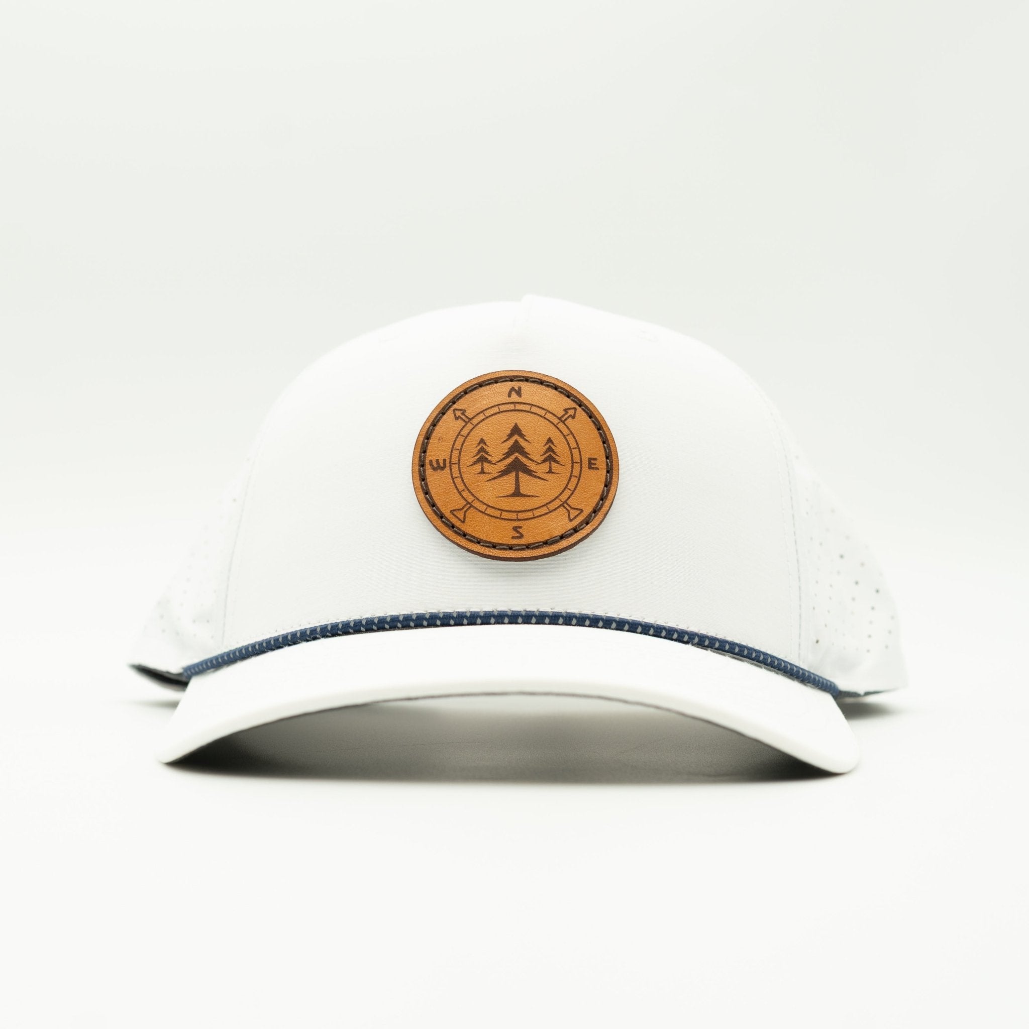 A white baseball cap with a curved brim, featuring a circular brown leather patch with a pine tree design on the front and a thin navy blue stripe along the edge of the brim.

Color: White/Navy