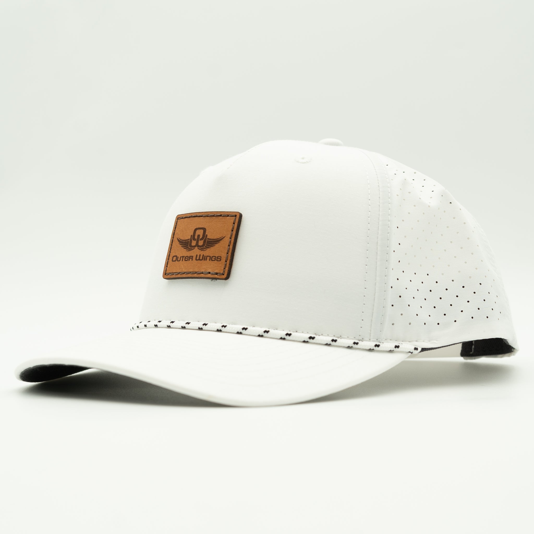 A white baseball cap with perforated side panels, a brown leather patch on the front featuring the 'Outer Wings' logo, and a decorative stitched line across the front of the brim, shown against a light gray studio background.

Color: Solid White