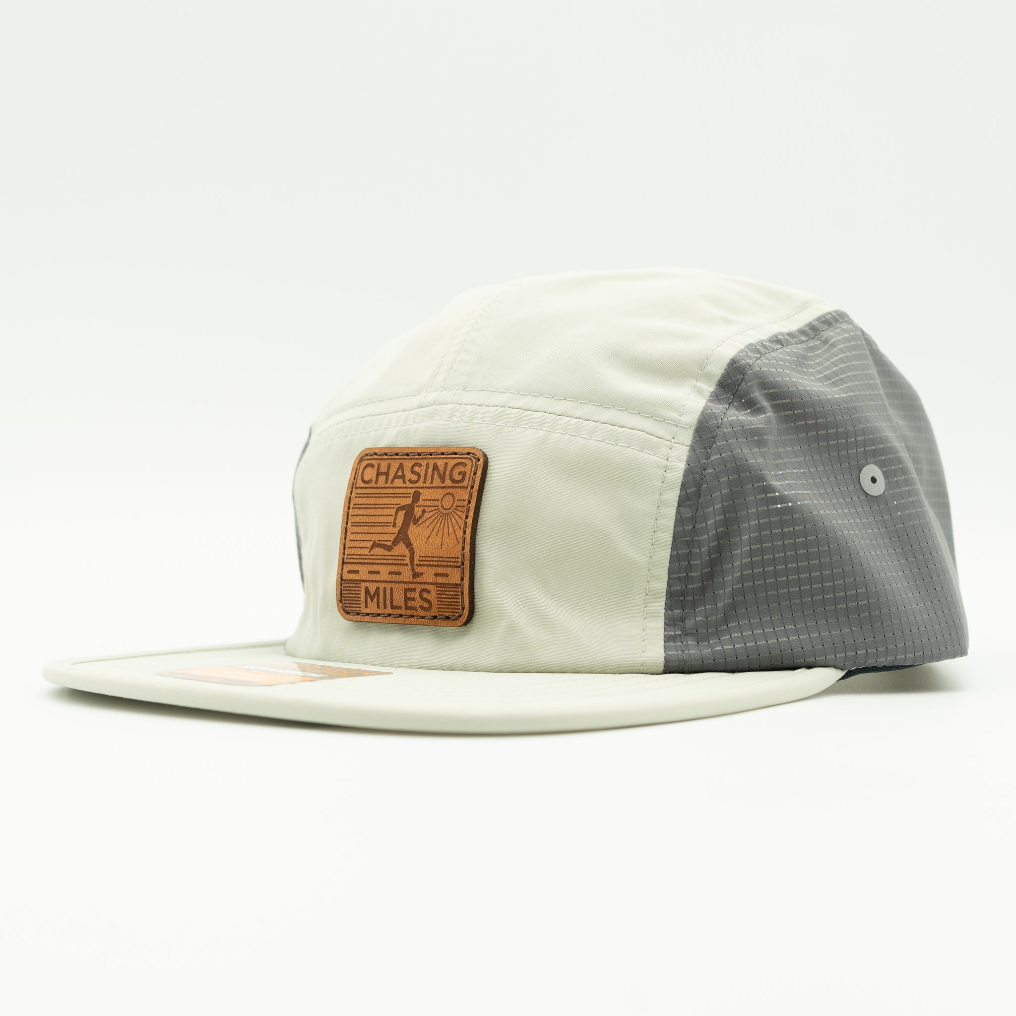 A 5-panel cap with a light cream front and brim, a dark gray mesh back, and a brown leather patch on the front that reads 'CHASING MILES'.

Color: Light Jade/Charcoal