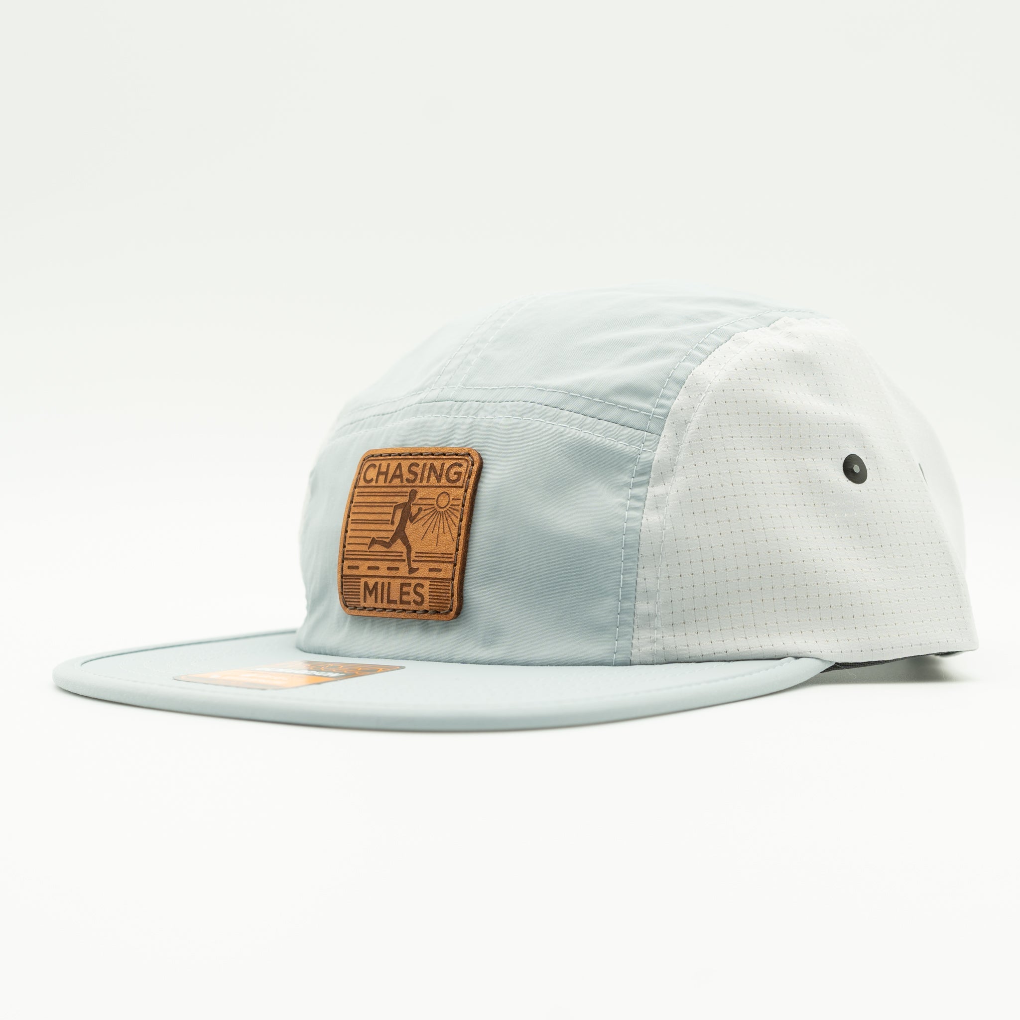 A light blue 5-panel cap with a brown leather patch on the front that reads 'CHASING MILES'.

Color: Grey/Glacier Grey