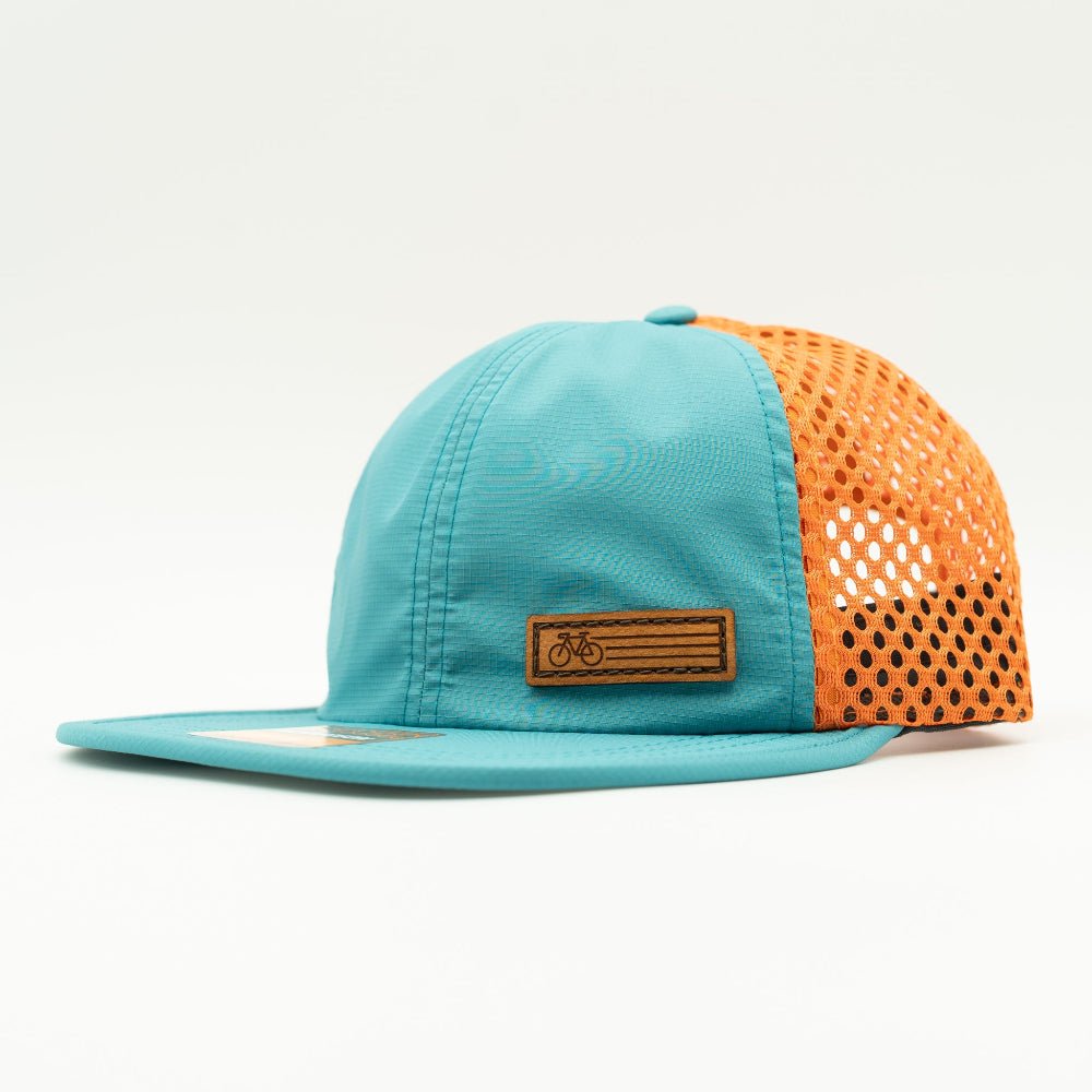 Side view of the Teal Fast Bike Hat, displaying the vibrant orange accents and wide-set mesh back, with the Fast Bike leather patch visible from the side.

Color: Teal/Orange