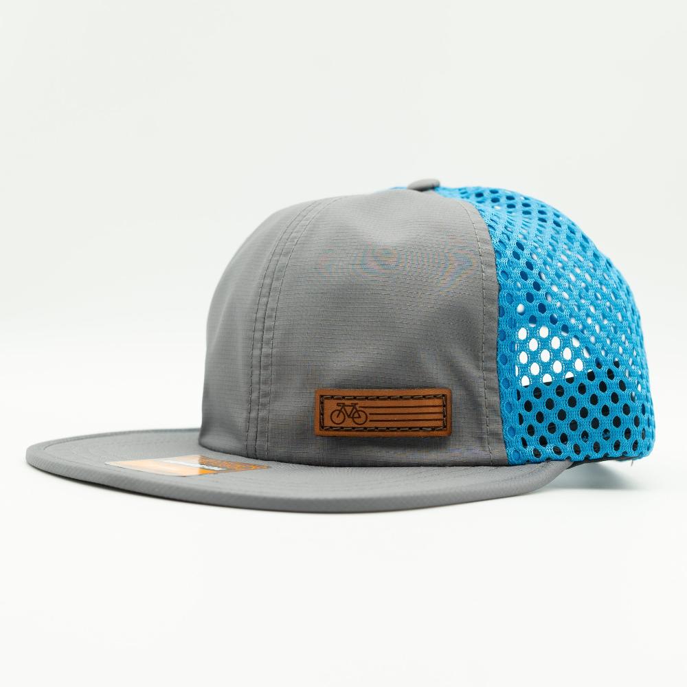 A gray flat-brim trucker cap with a bright blue perforated mesh back and a brown leather patch on the front.

Color: Charcoal/Cyan