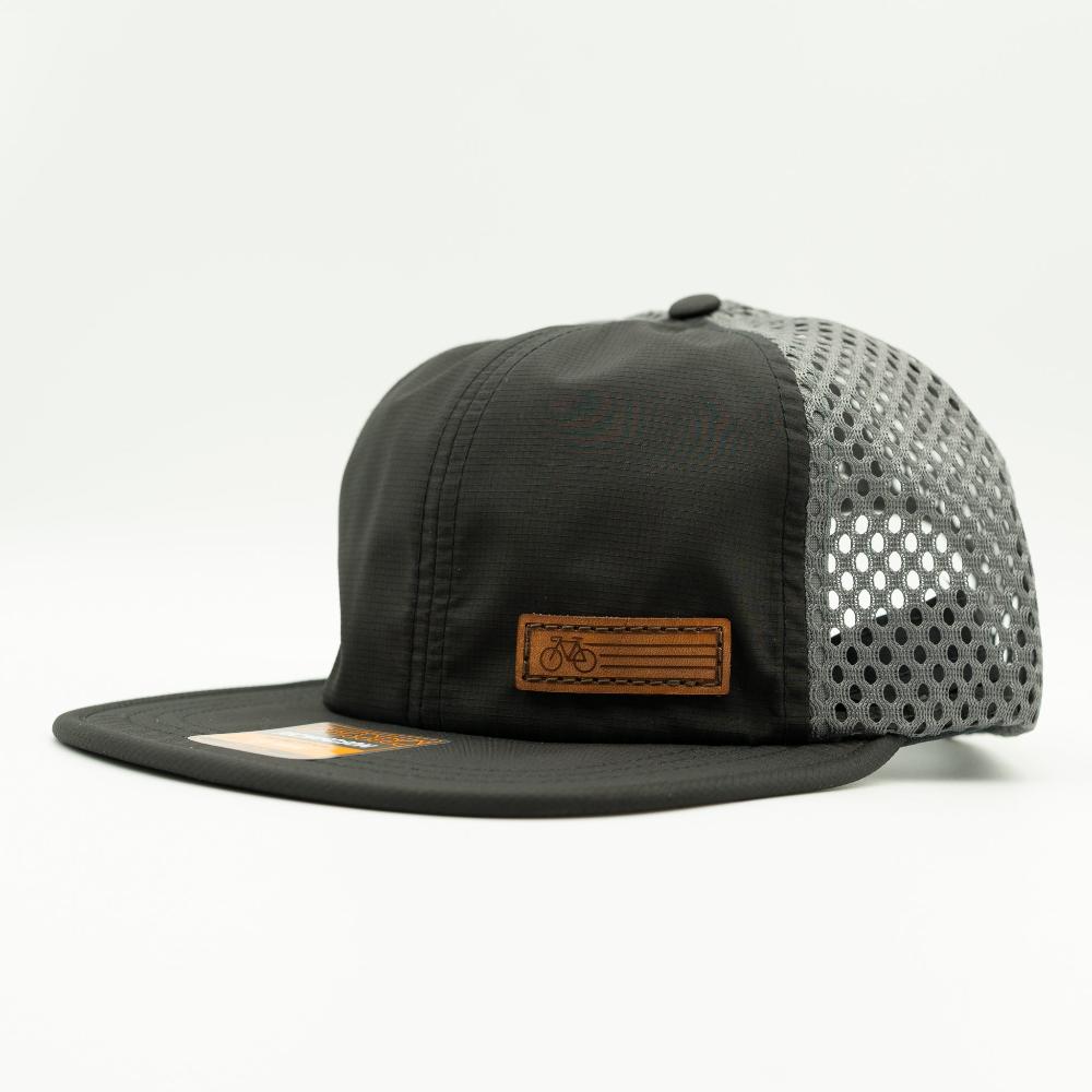 A black trucker-style cap with a structured black front panel and brim, black mesh side panels, and a brown leather patch on the front featuring a bicycle logo.

Color: Black/Charcoal